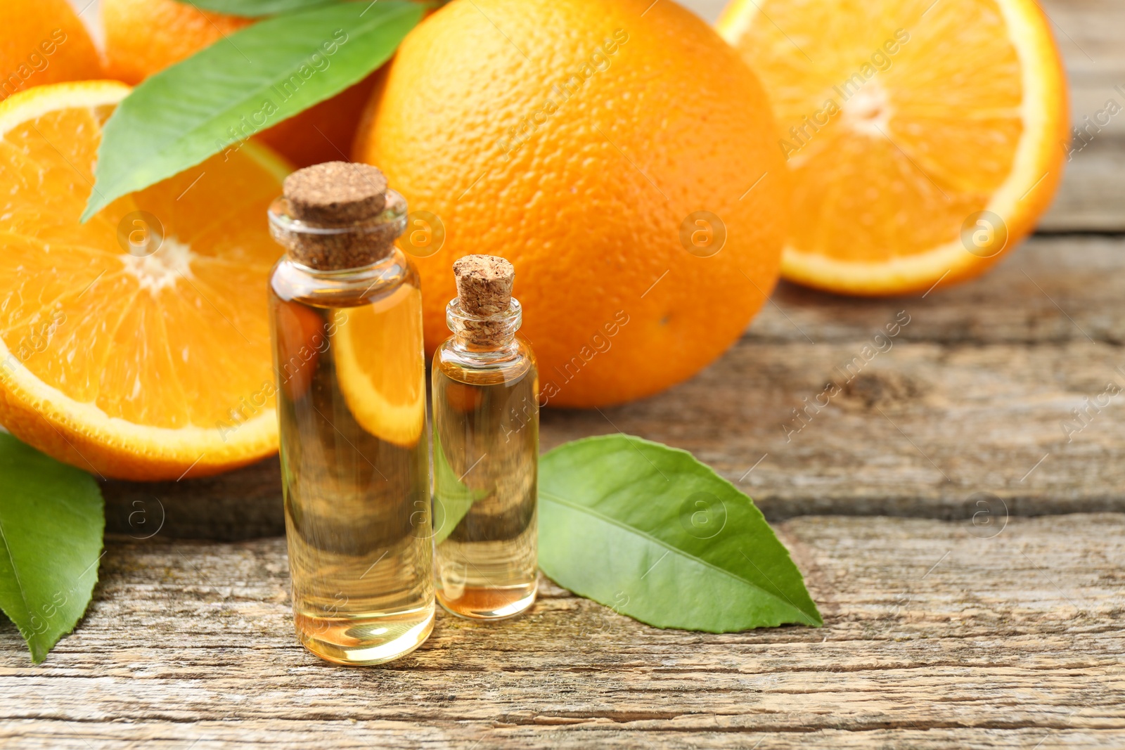 Photo of Essential oils in bottles, oranges and green leaves on wooden table