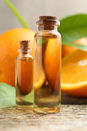 Essential oils in bottles and oranges on wooden table, closeup