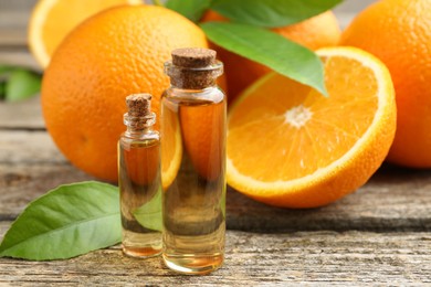 Essential oils in bottles, oranges and green leaves on wooden table, closeup