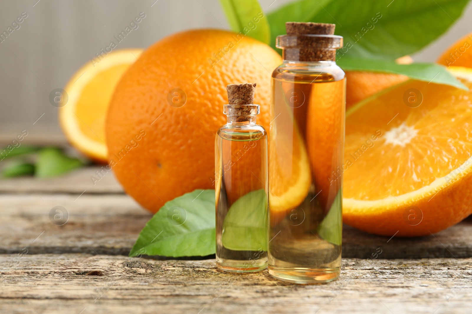 Photo of Essential oils in bottles, oranges and green leaves on wooden table, closeup