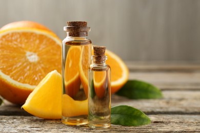 Essential oils in bottles, oranges and green leaves on wooden table, closeup