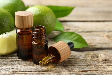 Essential oils in bottles, dropper, limes and green leaves on wooden table. Space for text