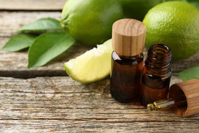 Essential oils in bottles, dropper, limes and green leaves on wooden table. Space for text