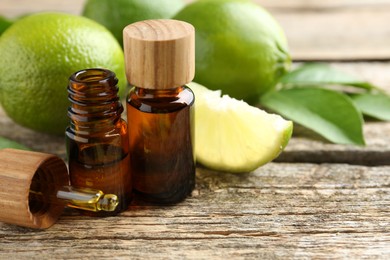 Essential oils in bottles, dropper, limes and green leaves on wooden table. Space for text