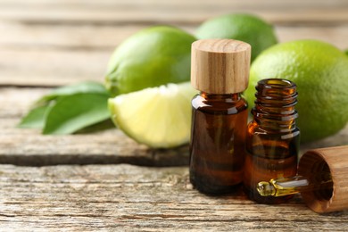 Essential oils in bottles, dropper, limes and green leaves on wooden table. Space for text