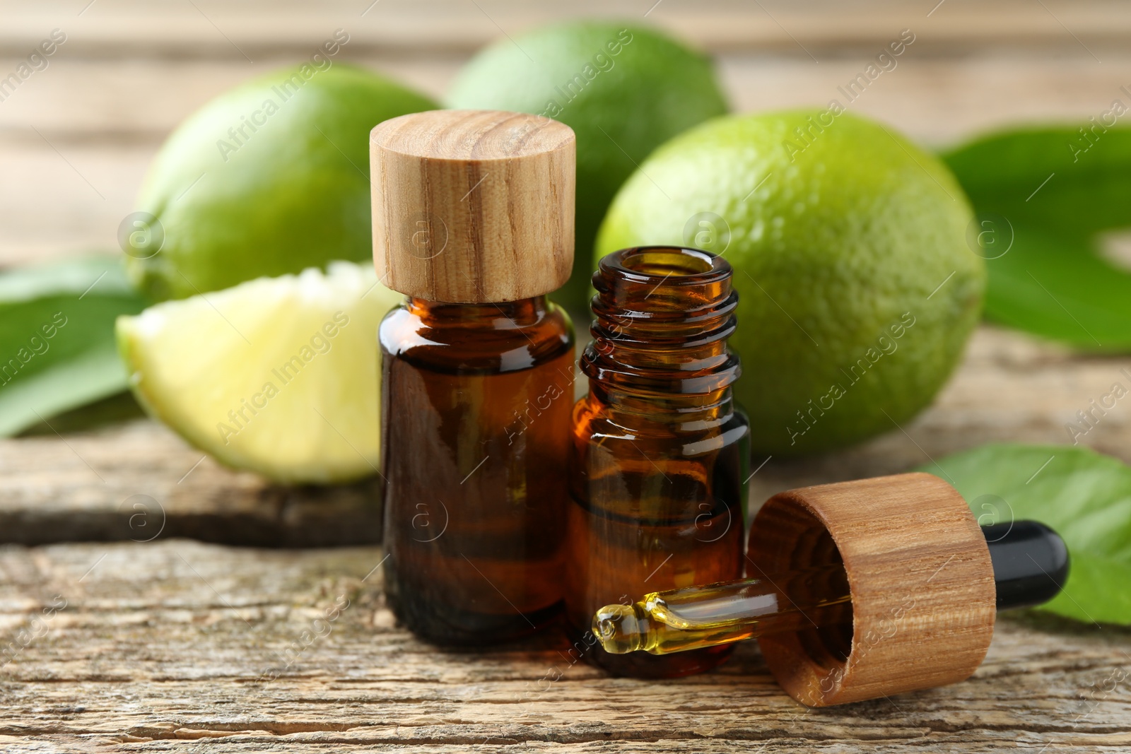 Photo of Essential oils in bottles, dropper, limes and green leaves on wooden table, closeup