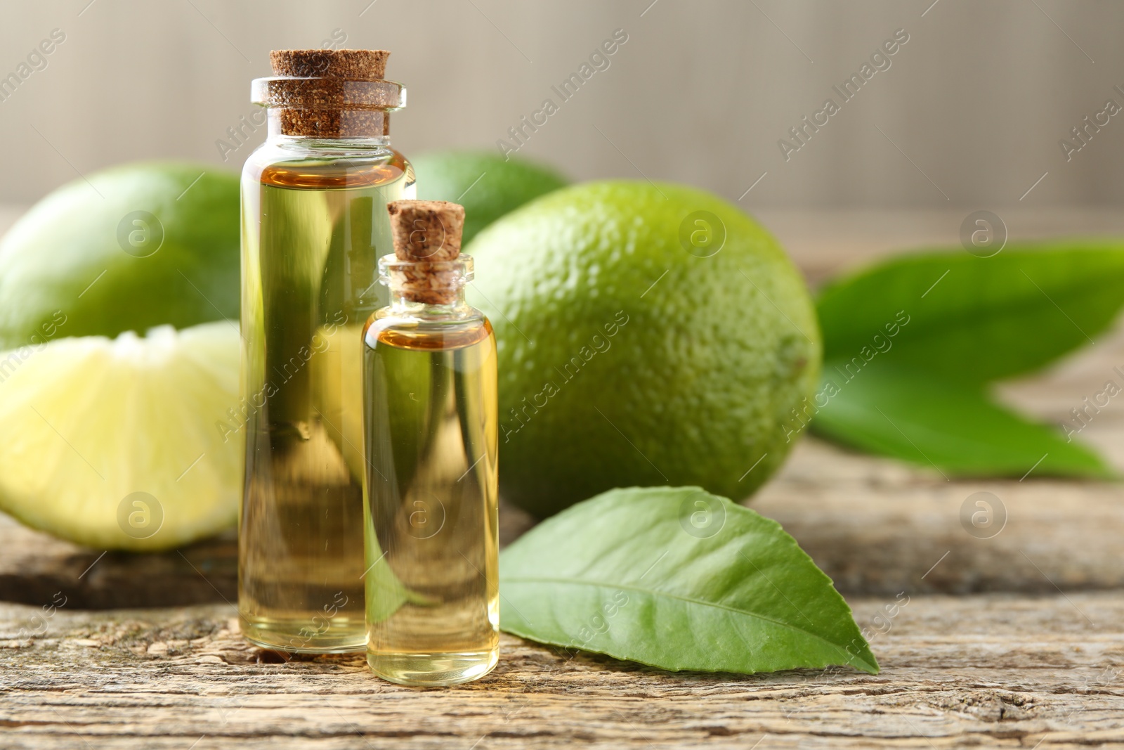 Photo of Essential oils in bottles, limes and green leaves on wooden table, closeup