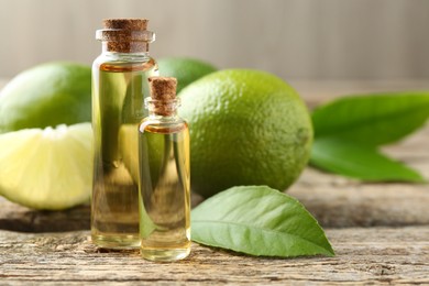 Essential oils in bottles, limes and green leaves on wooden table, closeup