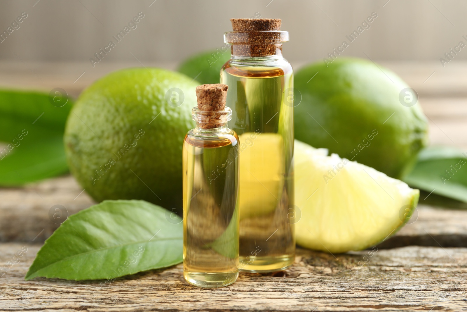 Photo of Essential oils in bottles, limes and green leaves on wooden table, closeup