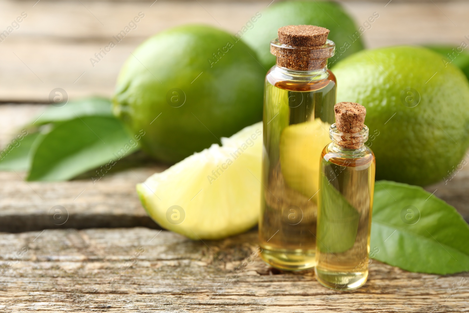 Photo of Essential oils in bottles, limes and green leaves on wooden table, closeup