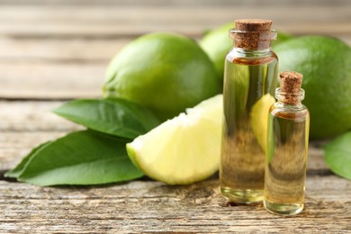 Essential oils in bottles, limes and green leaves on wooden table, closeup