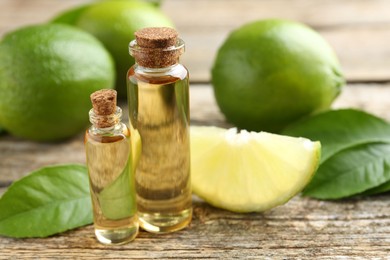 Essential oils in bottles, limes and green leaves on wooden table, closeup