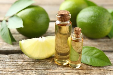 Essential oils in bottles, limes and green leaves on wooden table, closeup