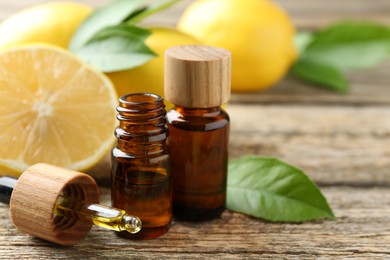 Essential oils in bottles, dropper, lemons and green leaves on wooden table, closeup