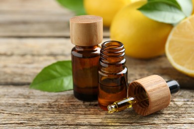 Essential oils in bottles, dropper, lemons and green leaves on wooden table, closeup