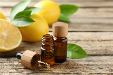 Essential oils in bottles, dropper, lemons and green leaves on wooden table