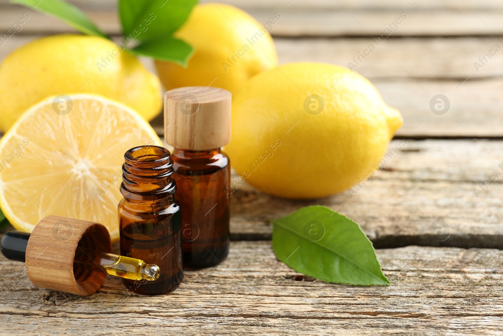 Photo of Essential oils in bottles, dropper, lemons and green leaves on wooden table