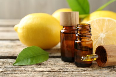 Essential oils in bottles, dropper, lemons and green leaves on wooden table, closeup