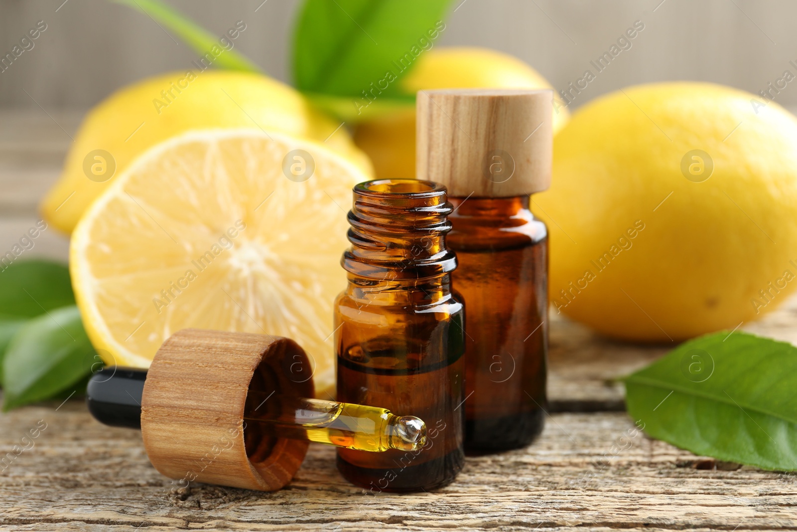 Photo of Essential oils in bottles, dropper, lemons and green leaves on wooden table, closeup