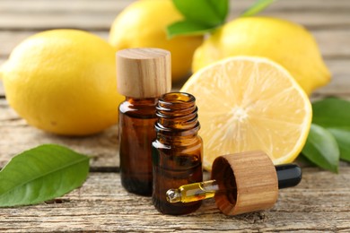 Essential oils in bottles, dropper, lemons and green leaves on wooden table, closeup