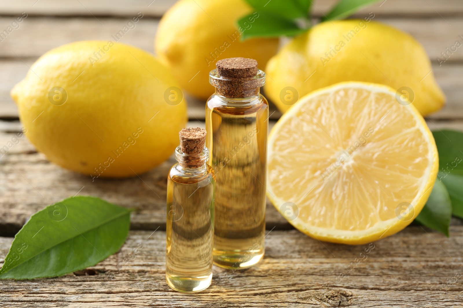 Photo of Essential oils in bottles, lemons and green leaves on wooden table, closeup