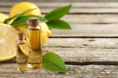 Photo of Essential oils in bottles, lemons and green leaves on wooden table, space for text