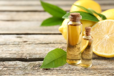 Photo of Essential oils in bottles, lemons and green leaves on wooden table, space for text