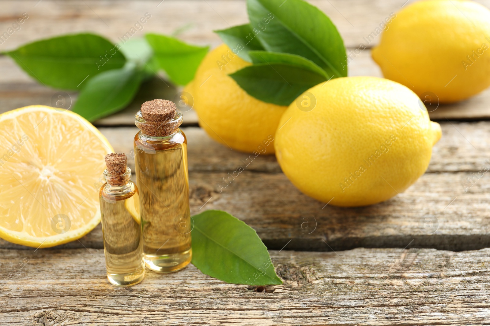 Photo of Essential oils in bottles, lemons and green leaves on wooden table