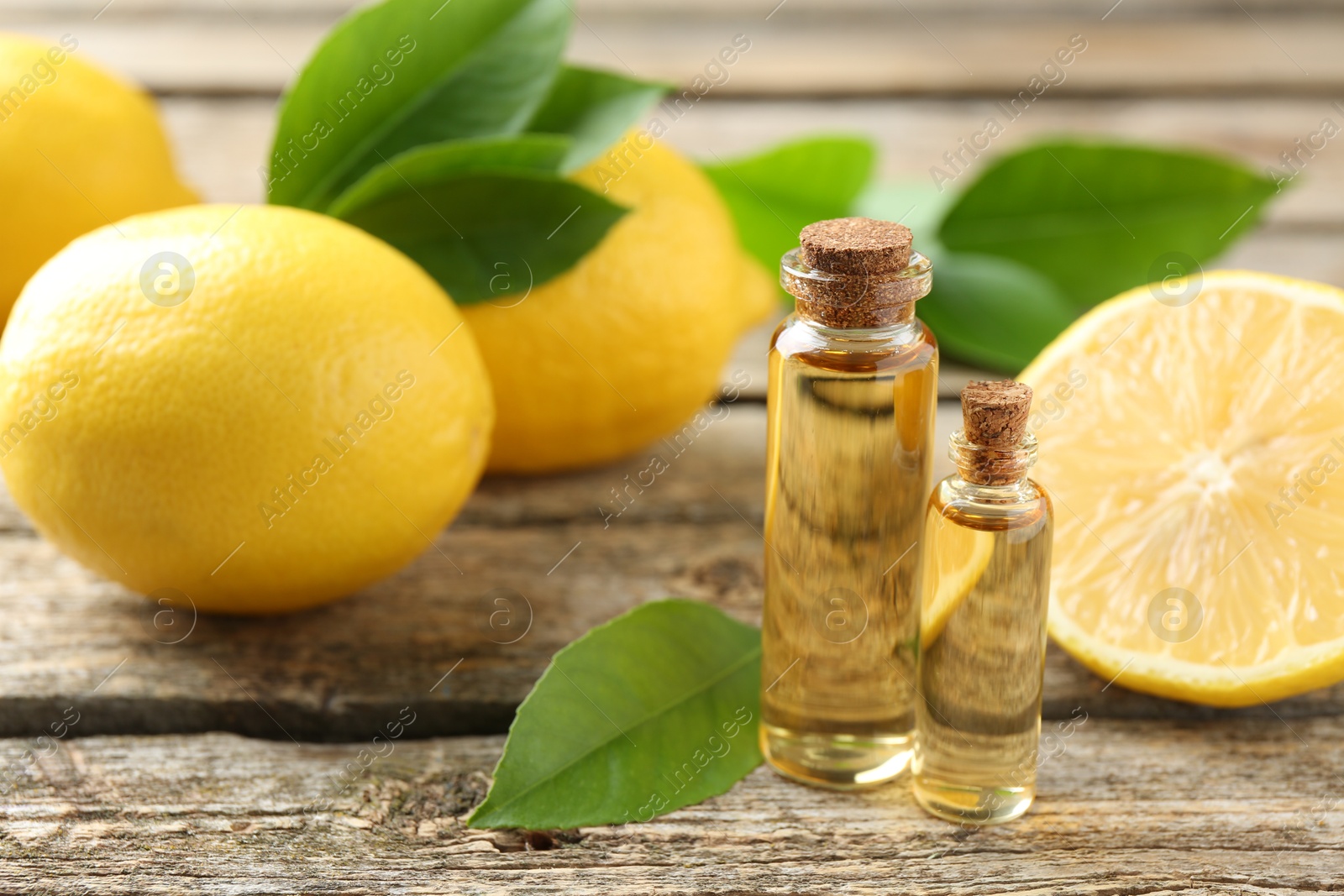 Photo of Essential oils in bottles, lemons and green leaves on wooden table