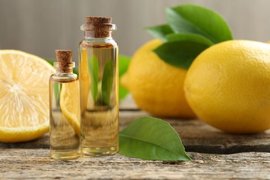 Essential oils in bottles, lemons and green leaves on wooden table, closeup