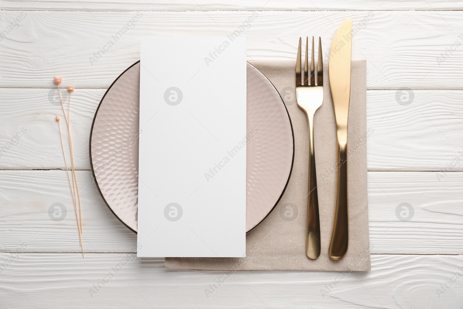 Photo of Empty menu, cutlery, plate, napkin and floral decor on white wooden table, top view. Mockup for design