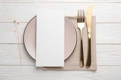 Empty menu, cutlery, plate, napkin and floral decor on white wooden table, top view. Mockup for design