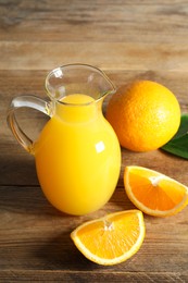 Photo of Tasty orange juice in glass jug and fresh fruits on wooden table