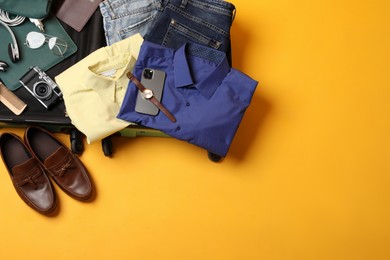 Open suitcase with traveler's belongings on yellow background, flat lay. Space for text