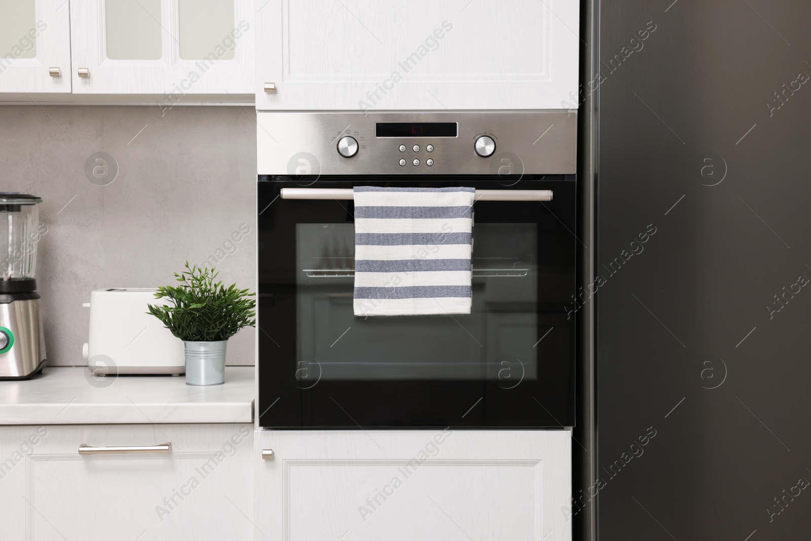 Photo of Electric oven with striped towel in kitchen. Cooking appliance