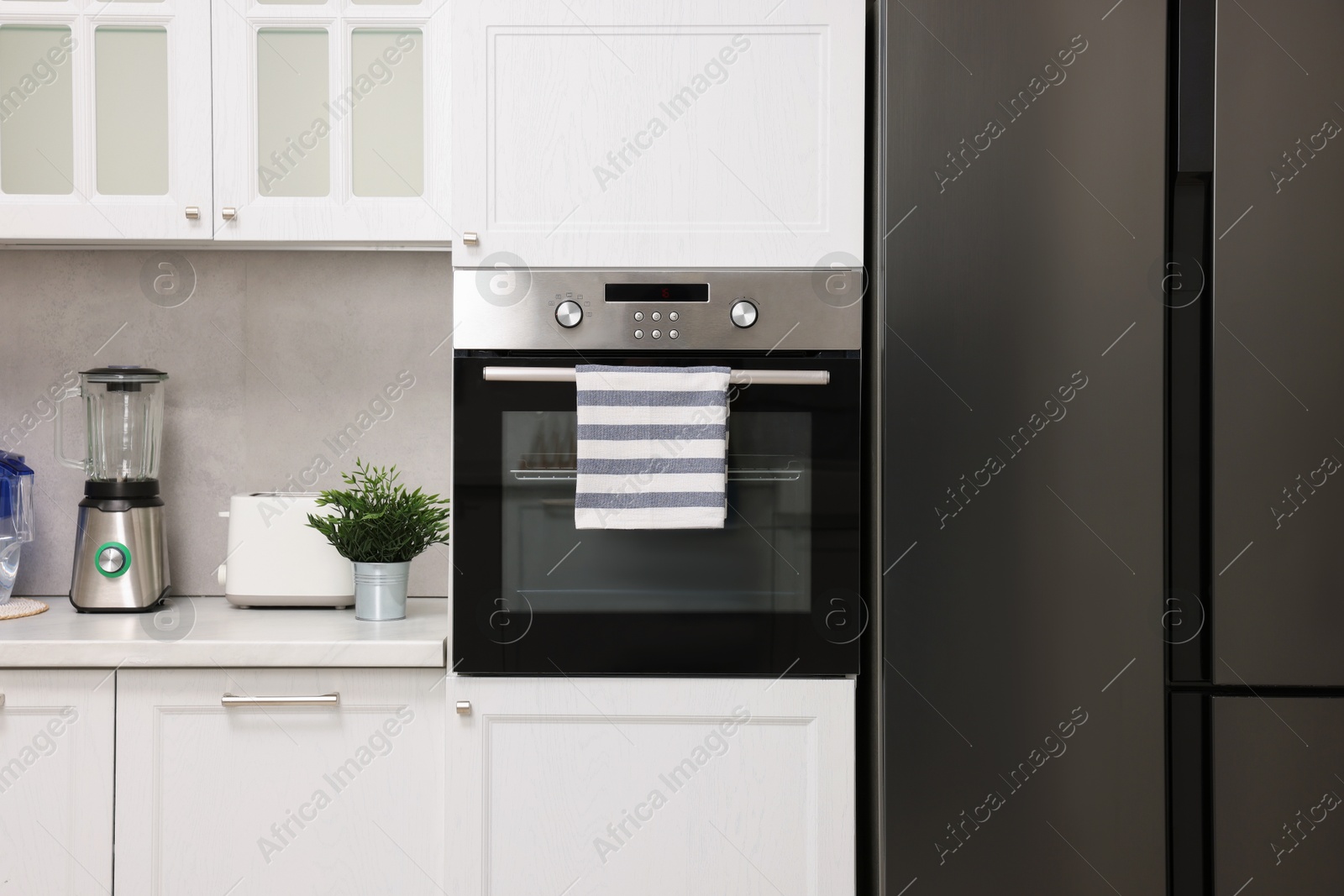 Photo of Electric oven with striped towel in kitchen. Cooking appliance