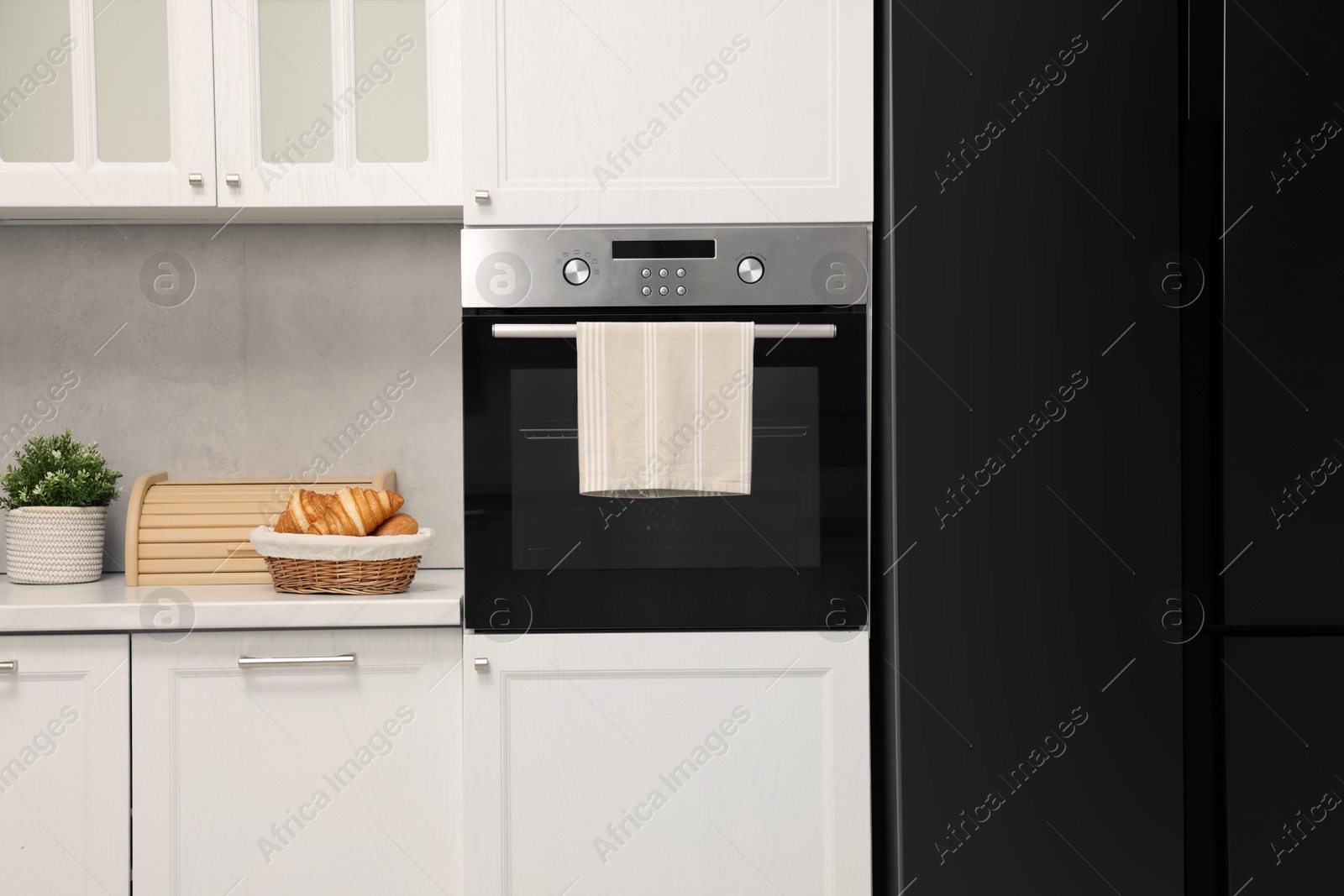 Photo of Electric oven with towel and croissants in kitchen. Cooking appliance