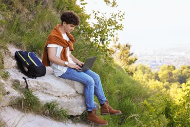 Travel blogger with backpack using laptop outdoors, space for text