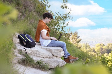 Photo of Travel blogger with backpack using laptop outdoors