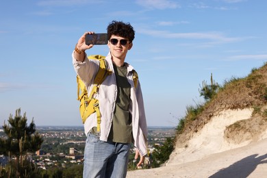 Photo of Travel blogger in sunglasses with smartphone streaming outdoors