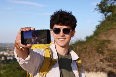 Travel blogger in sunglasses with smartphone streaming outdoors, selective focus