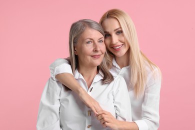 Family portrait of young woman and her mother on pink background