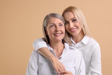 Family portrait of young woman and her mother on beige background