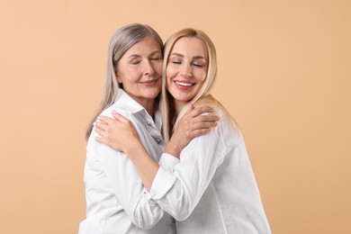 Family portrait of young woman and her mother on beige background