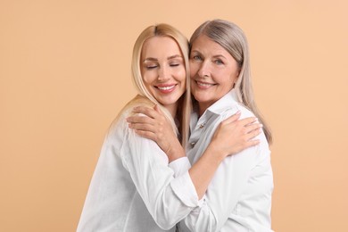 Family portrait of young woman and her mother on beige background