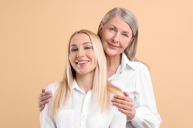 Family portrait of young woman and her mother on beige background