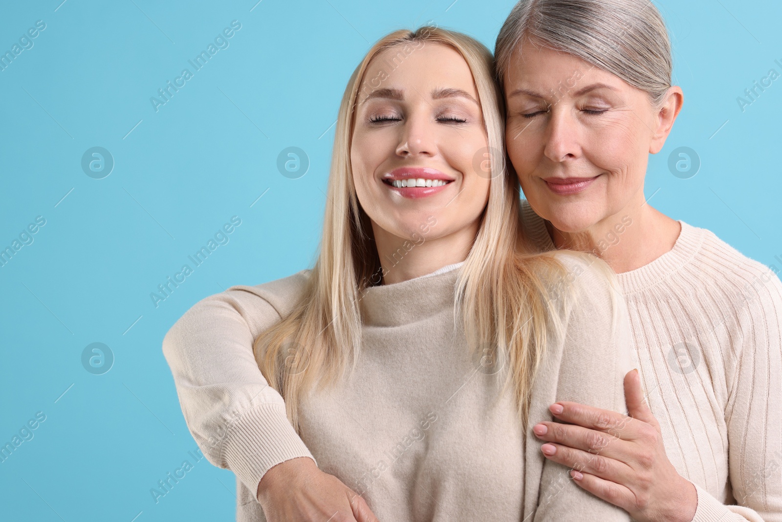 Photo of Family portrait of young woman and her mother on light blue background. Space for text