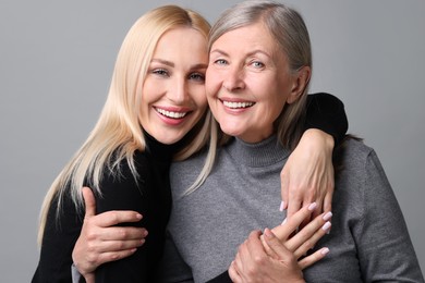 Family portrait of young woman and her mother on grey background