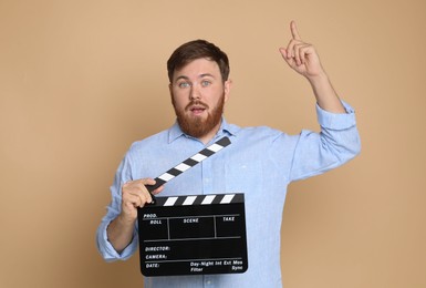 Making movie. Man with clapperboard pointing at something on beige background