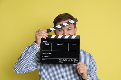 Making movie. Man with clapperboard on yellow background